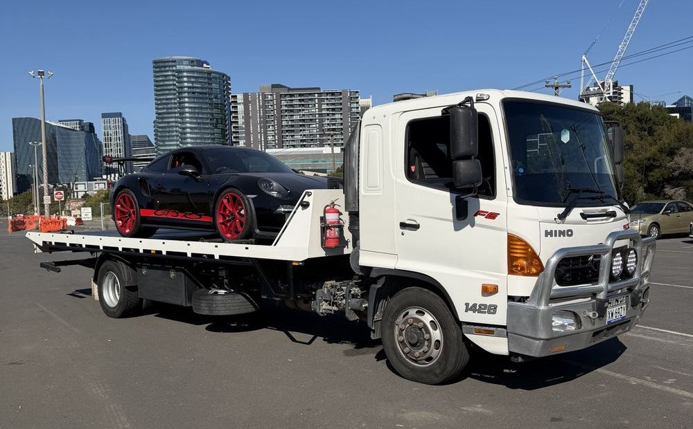 Hilly's flatbed tilt-tray truck carrying a black sports car with the Melbourne skyline behind