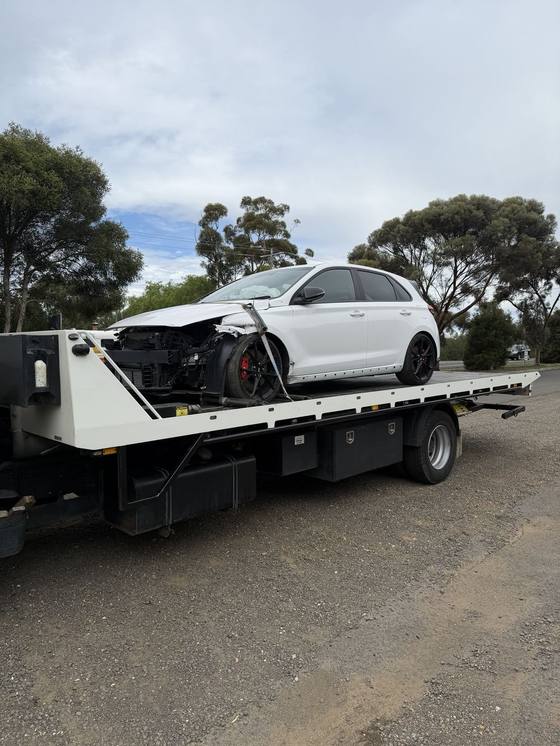 Hilly's truck carrying a white hatchback with front-end collision damage